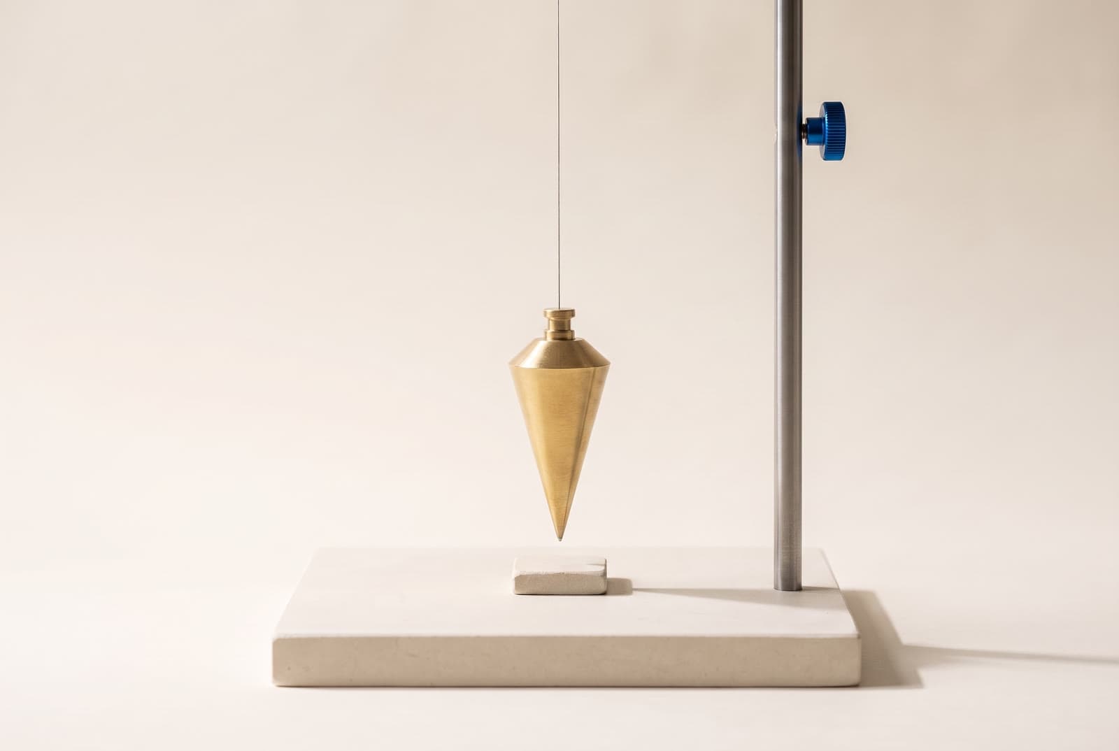 A brass plumb bob hanging still above a stone marker