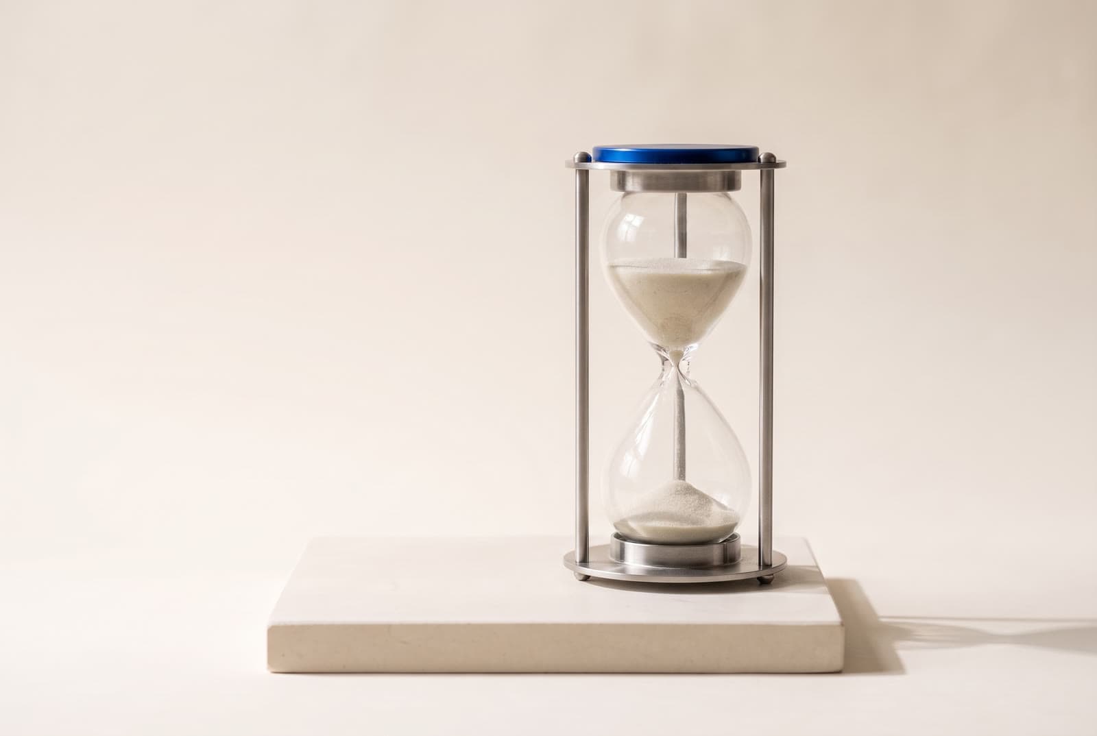 A steel-framed hourglass with fine sand mid-flow, on a stone plinth