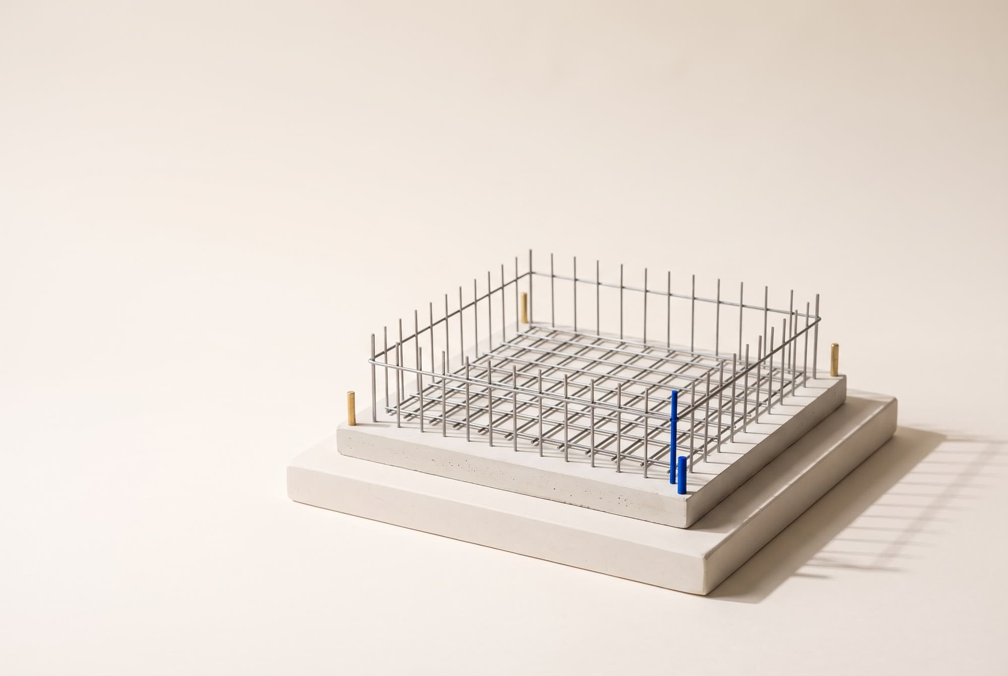 A white architectural maquette of a foundation slab with a steel rebar grid and one cobalt survey pin